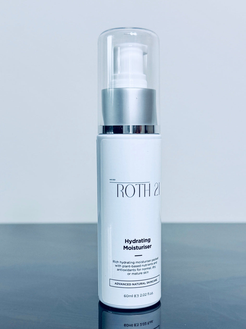 Skincare bottle with silver cap on a reflective surface and light gray background