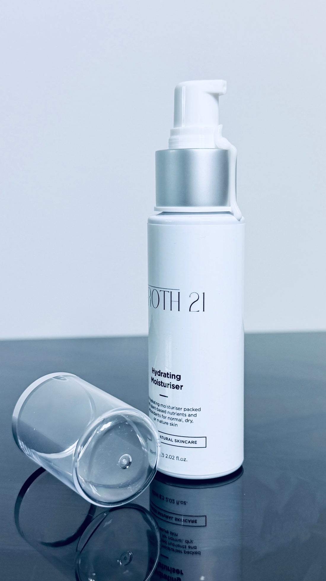 Skincare bottle with silver cap on a reflective surface and light gray background